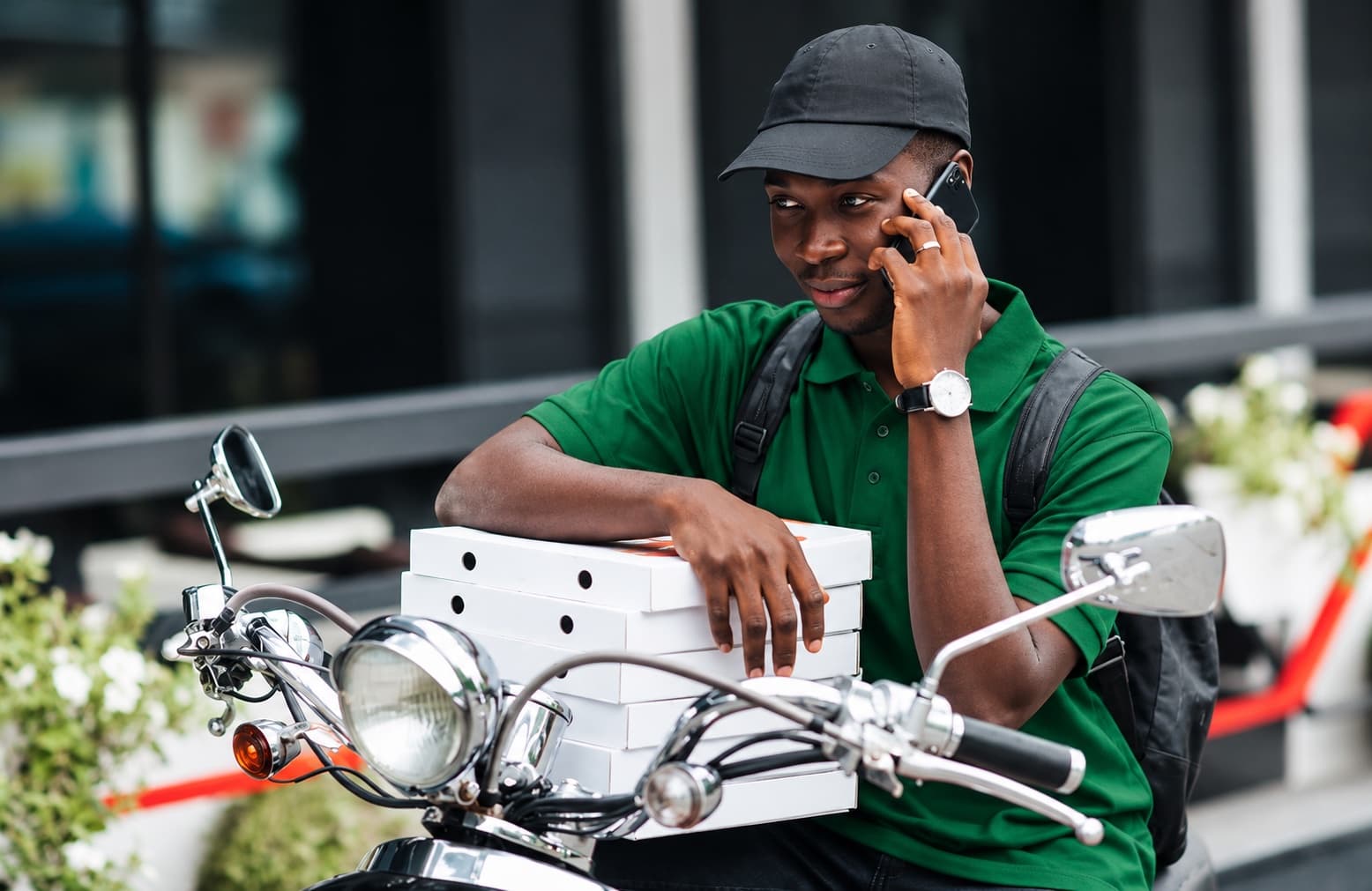 A delivery rider on his motorbike, on the phone, with orders stacked in front of him