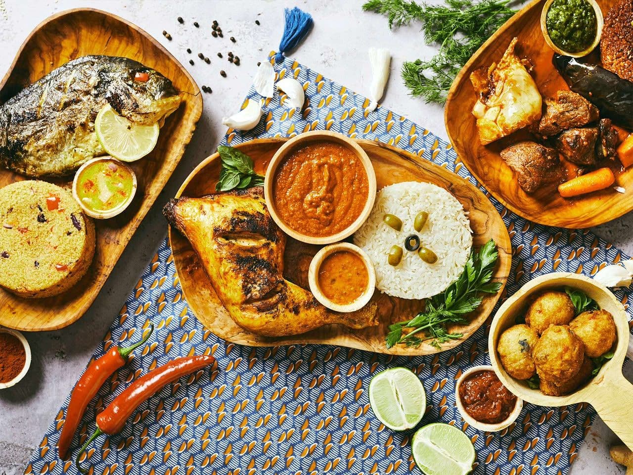 Une table de plats ouest-africains : poulet grillé avec du riz et ses sauces, poisson braisé, viande en sauce et beignets